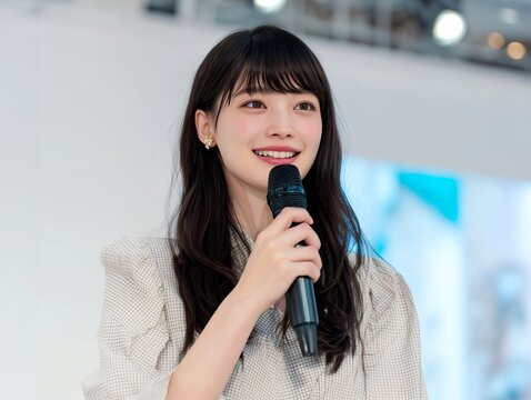 マイクを手に笑顔で話す若い女性がイベントで想いを伝える発表シーン写真