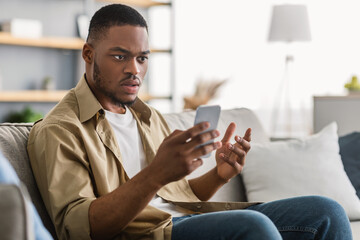 Shocked African American Man Using Smartphone Having Problem With Mobile Application Sitting On...