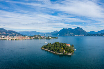 Obraz premium A wide aerial perspective captures Isola Madre surrounded by the deep blue waters of Lake Maggiore, with distant towns, forested hills, and rugged alpine mountains under a sky streaked with soft