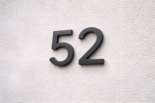 Sleek black numeral '52' prominently displayed on a bright, textured white wall, representing a house number, address marker, or abstract numerical concept