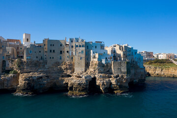 Clustered stone and whitewashed buildings perch atop rugged limestone cliffs overlooking the deep blue Adriatic Sea in Polignano a Mare, Apulia, Italy. The coastal scene is defined by textured rock