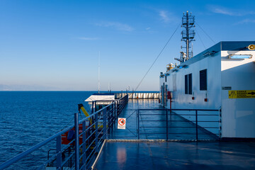 Open ferry deck with metallic railings and white structure under clear morning light, overlooking...