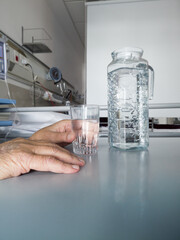 Hand of an elderly patient holding a glass of water on a hospital table