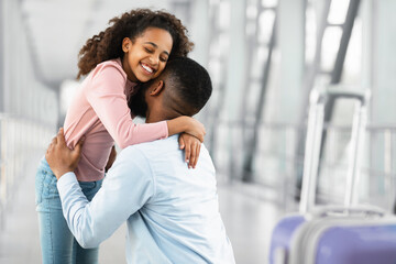 Meeting In Airport Concept. Little black girl embracing her happy father after arrival in airport, returning back home from vacation journey voyage, back view of man hugging daughter. Homecoming