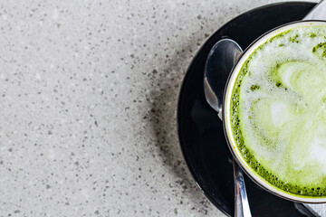 Top view of a half hot matcha latte in the black mug or cup. flat lay. high angle, above. spoon. stainless steel. tissue. table. grey or gray. white. green. copy space, empty, free, negative, text, de