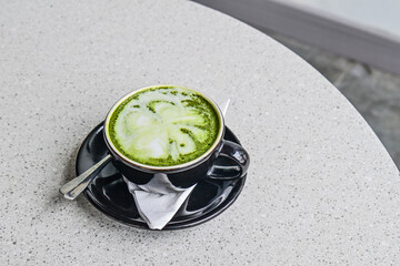 Close up view of hot matcha latte in the black mug or cup. spoon. stainless steel. tissue. table. grey or gray. white. green. copy space, empty, free, negative, text, design. granite table.