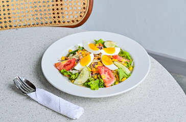 close up view of egg salad on the white plate. cruttong. mix salad. boiled egg. dressing. vegetables. high angle, above. granite table on the background. spoon, fork and tissue. stainless steel. grey.