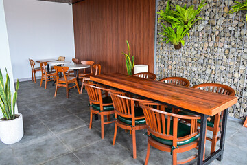 Empty long wooden table And chairs. grey or gray rocks on the wall. outdoor seating for restaurant, Cafe or coffee shop. Plants, leaves, green, nature, wall. wood. brown. trellis. hanging, hang.