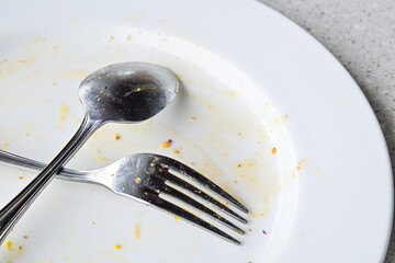 Empty plate with leftover food and utensils after a meal. extreme close up view. isolated. granite table on the background. fork and spoon. stainless steel. crossed, cross. x. leftovers. eat, eating.
