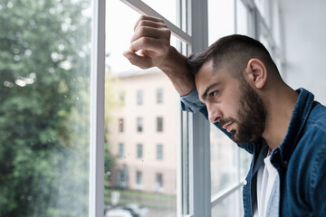 Dramatic portrait of caucasian man, alone by window at home looking sorrow with desperate feeling...