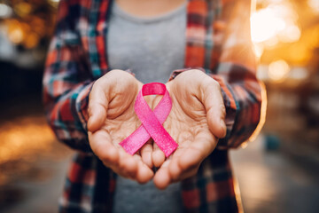 woman holding pink cancer awareness ribbon in warm sunlight background.