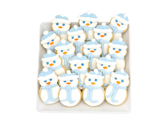 Top above view of square porcelain plate filled with homemade sugar cookies snowmen with marshmallow fondant and royal icing. Isolated on white background