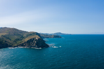 Sweeping view of a rugged headland jutting into vivid blue Mediterranean waters near Banyuls-sur-Mer, with sunlit hillsides and open sky creating a sense of freedom and natural beauty.