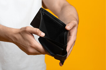 Financial crisis and bankruptcy while COVID-19 pandemic concept. Unrecognizable man showing empty wallet at camera, short of money, yellow studio background, copy space, cropped shot