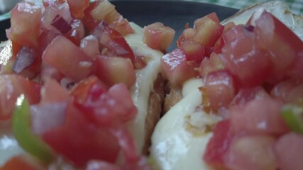 Close-up pull away of delicious traditional Mexican mollete sandwiches served on a plate with melted cheese, pico de gallo, diced tomatoes and vegetables