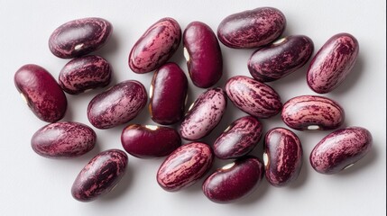 Close-up shot of a scatter of speckled, oval-shaped legumes. They vary in deep burgundy and pink hues, with distinct white markings, arranged on a white surface