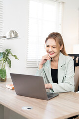 Happy Asian businesswoman in a green blazer talking on a smartphone, reviewing documents, and...