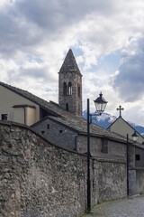Fototapeta premium Medieval stone church and bell tower of Sant'Orso in Aosta, Italy. Traditional architecture framed by alpine peaks, clouds and mountain landscape.