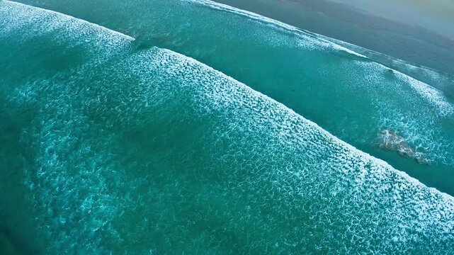 Aerial of turquoise ocean waves rolling in parallel lines along rugged coastline at Wilsons Promontory, angled overview, Victoria Australia
