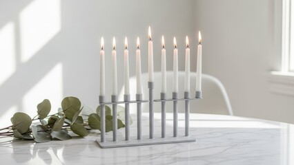 Modern gold Hanukkah menorah with nine lit white candles on a marble table with eucalyptus leaves. Minimalist Jewish holiday home decor, festive Hanukkiah lighting, and Chanukah celebration.