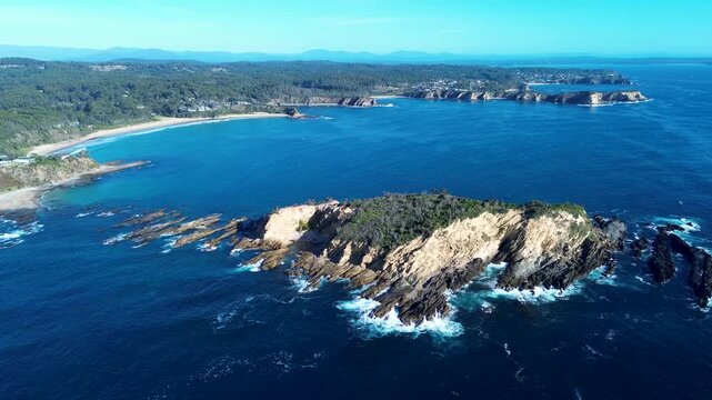 Drone aerial landscape of ocean waves crashing along Jimmies Island headland with Rosedale beach and surrounding rural suburbs in Malua Bay coastline South Coast Australia travel tourism nature
