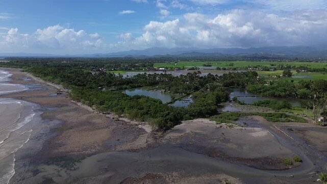 Scenic aerial drone footage of Roxas in Oriental Mindoro, Philippines showing sandy beaches, green rice fields and mountains in the background, perfect tropical landscape view.