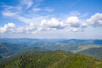 Fototapeta premium Vast panorama of rolling forested hills and distant blue mountains beneath a sky filled with dramatic white clouds in the Ardeche region.