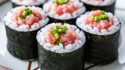 Close-up of negitoro sushi rolls made with minced tuna, rice, and seaweed, topped with fresh green onion on a plate.