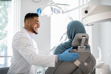 Obraz premium Dental Treatment. Arab Dentist Doctor Making Check Up To Muslim Female Patient In Stomatological Clinic, Middle Eastern Stomatologist Consulting Islamic Woman In Hijab During Appointment, Free Space