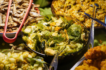 Assorted traditional Indonesian dishes with vibrant homemade flavors, mixed vegetables, fried fish, savory side dishes, and rustic market-style presentation, rich cultural culinary visuals