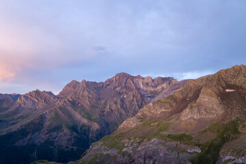 Gentle evening light illuminates the jagged peaks and rocky slopes of the Pyrenees, with subtle pastel hues in the sky creating a peaceful, atmospheric scene.