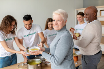 A happy elderly woman smiles as she receives soup from a volunteer group dedicated to helping...