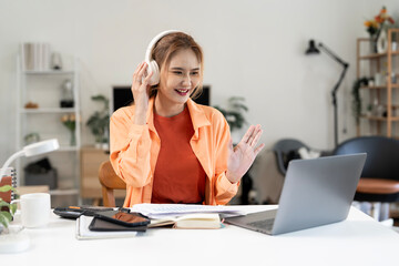 Happy Asian woman with headphones having a video call on a laptop at home. Concept of teleconference, online consulting, remote working, and e-learning.