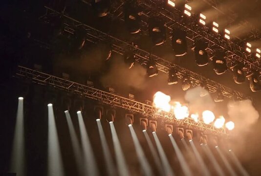 Stage pyrotechnics with fire flares and orange spotlights in concert hall lighting rig motion during music performance show spectacular entertainment production clip