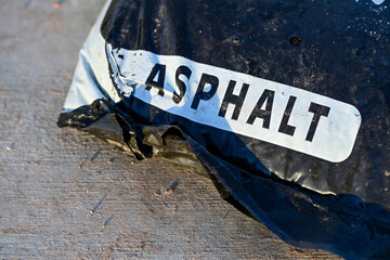 Close view of a labeled asphalt material bag on a paved surface, representing road construction supplies, pavement repair materials, and infrastructure maintenance operations