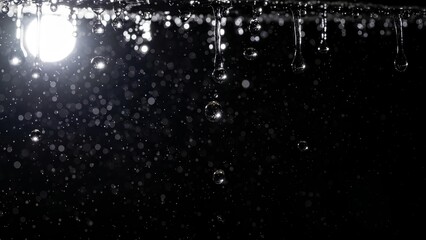 Close-up of water droplets falling from a surface with a bright light source in the background.