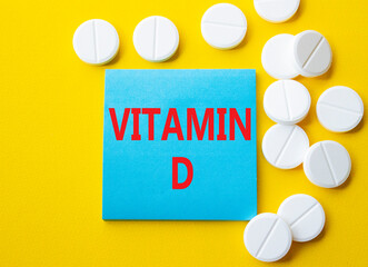 Vitamin D symbol. Concept word Vitamin D on blue note. Beautiful yellow background with pills. Medicine and Vitamin D concept. Copy space