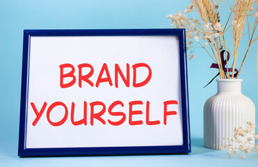 Brand yourself symbol. Concept words Brand yourself on beautiful wooden picture frame. Beautiful light blue background with flower vase. Business and Brand yourself concept. Copy space.