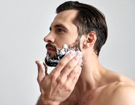 Man applying shaving cream to beard, facing left, against a white backdrop