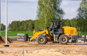 Heavy orange wheeled loader transporting pallet with concrete blocks attached. Worksite outdoors. Construction and renovation concept. Auto loader with aerated concrete blocks.