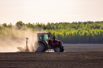 Obraz premium Tractor plowing field at sunset. Red tractor plowing, cultivating soil. Plow on plowed. Farm tractor on cultivated field for sowing seeds. Grain deal on field cultivation. Plowed field.