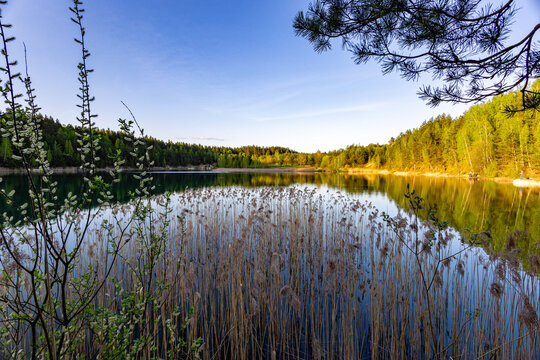Still waters of a quarry lake and lush greenery surrounding it, creating a peaceful atmosphere. The fading light casts a gentle glow on the tranquil landscape.