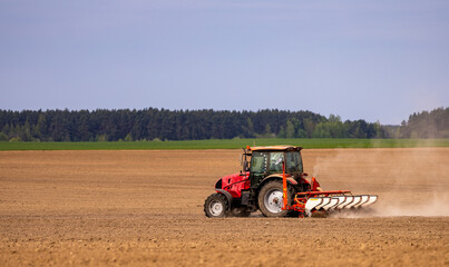 Obraz premium Farmer in tractor preparing farmland with seedbed for the next year. Powerful tractor at work, turning over soul on a vast farmland under a clear sky.