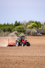 Obraz premium Farmer in tractor preparing farmland with seedbed for the next year. Powerful tractor at work, turning over soul on a vast farmland under a clear sky.