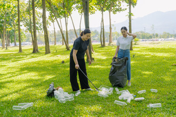 Two Asian women are picking up litter on the lawn in a park, participating in a daytime environmental cleanup.