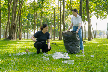 Two Asian women are picking up litter on the lawn in a park, participating in a daytime environmental cleanup.
