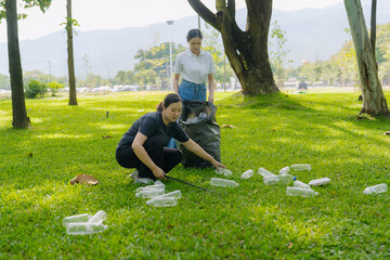 Two Asian women are picking up litter on the lawn in a park, participating in a daytime environmental cleanup.