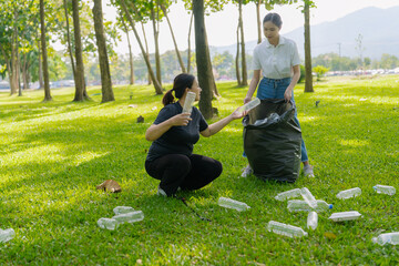 Two Asian women are picking up litter on the lawn in a park, participating in a daytime environmental cleanup.