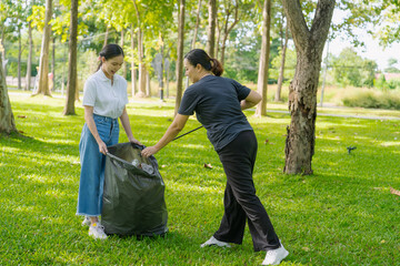 Two Asian women are picking up litter on the lawn in a park, participating in a daytime environmental cleanup.