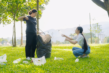 Two Asian women are picking up litter on the lawn in a park, participating in a daytime environmental cleanup.